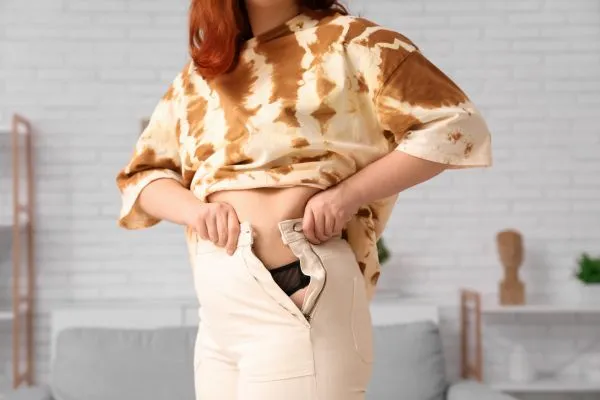 Image of woman trying to do her trousers up after pregnancy weight gain Preston